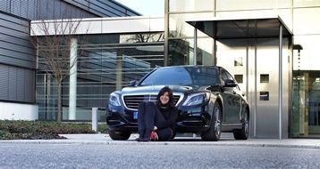 girl sitting on the ground near the black car