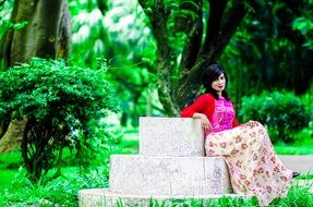 beautiful young girl sits on stone in green park