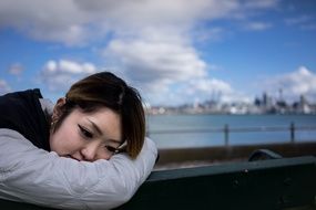 Asian woman sits on bench at water in city