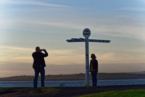 Man taking photo of woman at signpost, uk, scotland