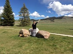girl stands near stones in a green meadow