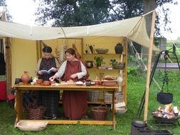 Roman Cooking, two young women beneath shed and pot above campfire