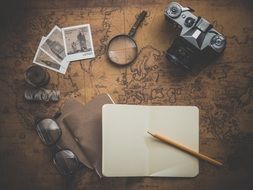 camera, notebook and glasses on the vintage map