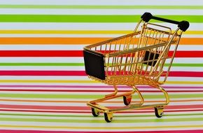 golden shopping trolley on the background of multicolored stripes