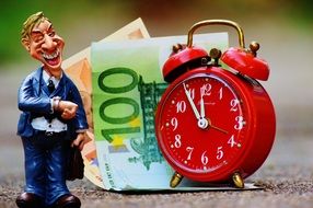 red alarm clock, figurine of businessman and banknotes