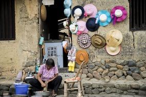 woman working in front of colorful womenâs Hats on stone wall