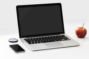 smartphone and red apple near laptop on a white table