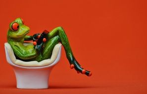 figurine of frog with gadget on cozy chair