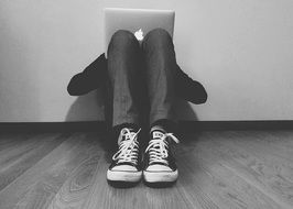 person in sneakers sitting on floor with apple Laptop