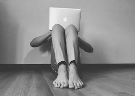 black and white photo of a young man with a laptop on the floor