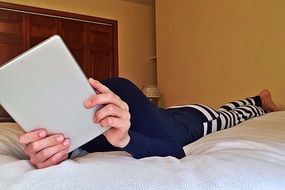 girl in pajamas looks at the tablet while lying on the bed