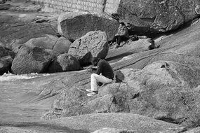 Black And White photo of man sitting on a rock