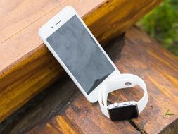 white Iphone and Iwatch on the wooden bench