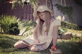 little girl reads a book in a green meadow