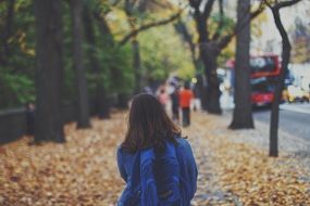 a girl with a backpack is on dry leaves