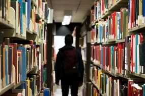 student in the library between shelves with books