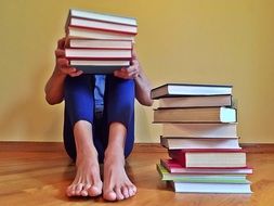 man sitting with a stack of books near the wall