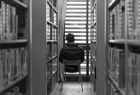 a young man sits on a chair between the bookshelves in the library