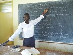 young dark skin man at blackboard in classroom, Chemistry Teacher, Uganda