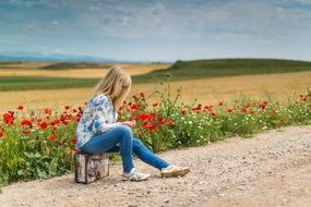 young girl sitting on a suitcase near the road