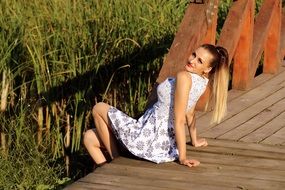 girl in a summer dress sits on a wooden pier