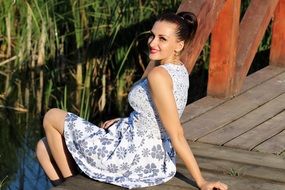 smiling Girl sits on wooden Bridge in short Dress