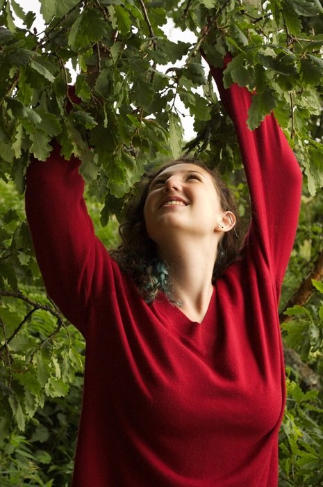 girl in a red sweater near a green tree