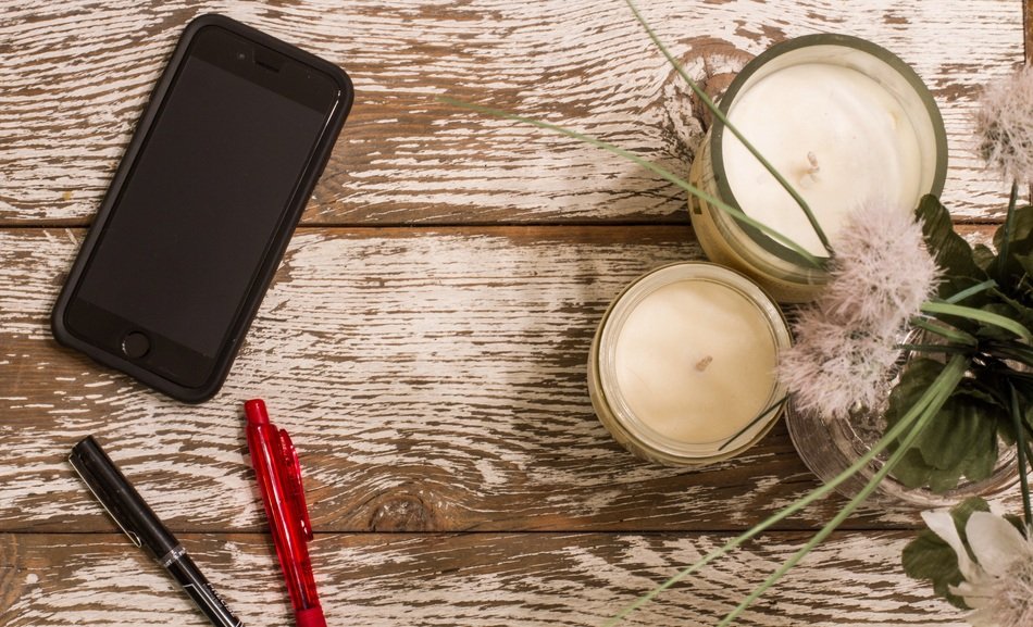 black smartphone, multi-colored pens and candles on the table