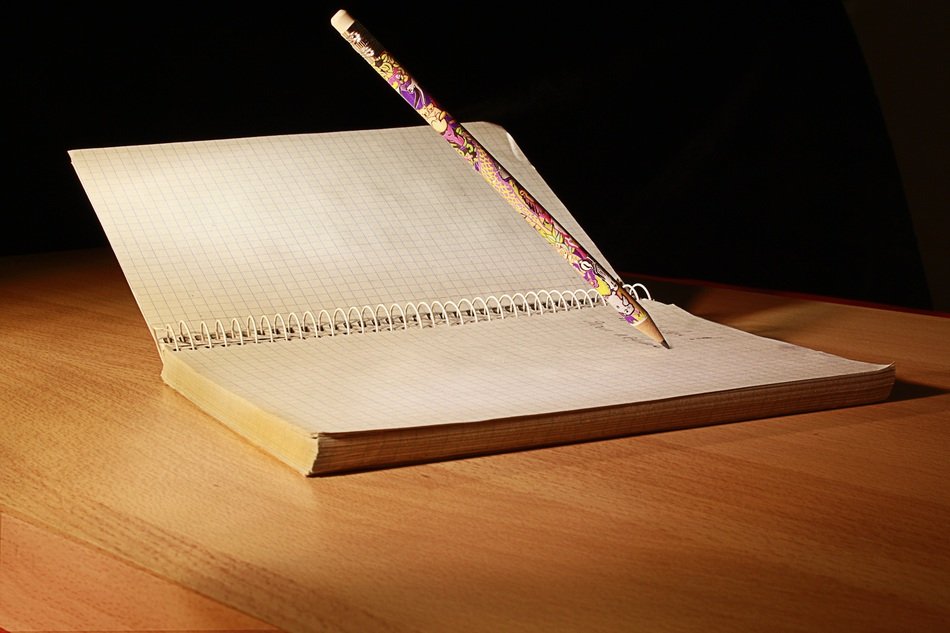 Pencil writting on old notebook lying on wooden table