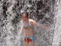 girl in a swimsuit stands under a waterfall