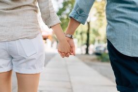 young couple is holding hands walking along the street