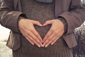 hands in the shape of a heart on the belly of a pregnant woman
