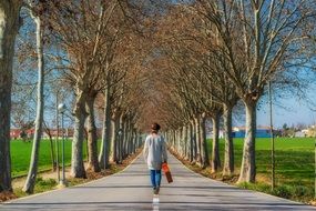 man walking along a road with trees at the edges