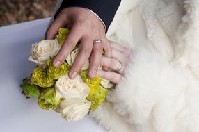 hands of the newlyweds on a wedding bouquet