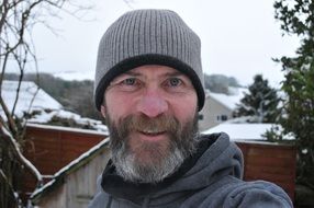 a man with a beard and a hat on the background of the village