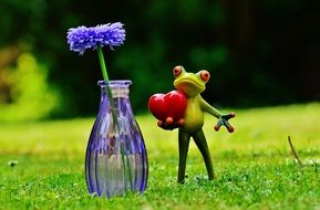 figure of a frog on green grass near a glass vase