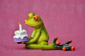 figure of the green frog with birthday cake on a pink background