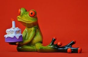 figure of the green frog with birthday cake on red background