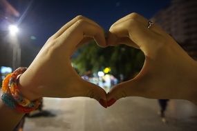 heart made of fingers on the background of a night park