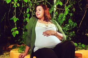 pregnant girl sits on the ground under a tree