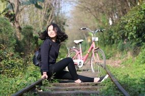 young asian Girl sits on railroad at pink Bike