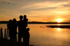 photo of a happy family by the sea on a background of golden sunset