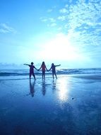 three friends hold hands on the beach