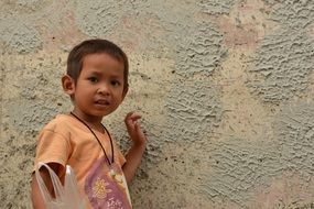 dark-skinned little boy stands near the wall