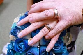 two hands of the bride and groom on a wedding bouquet