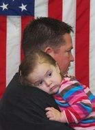 dad with daughter in his arms on the background of the american flag