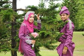 newlyweds in traditional dresses near the coniferous tree