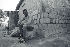 young man on a stone near a hut in black and white image