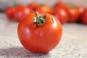 red Tomato on gey surface in front of distant tomatoes