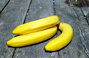 three yellow bananas on a wooden surface